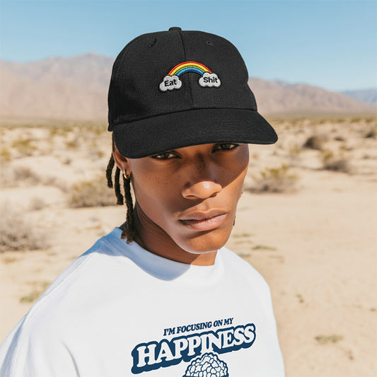 Person wearing a black cap with a rainbow design and text, standing in a desert landscape.