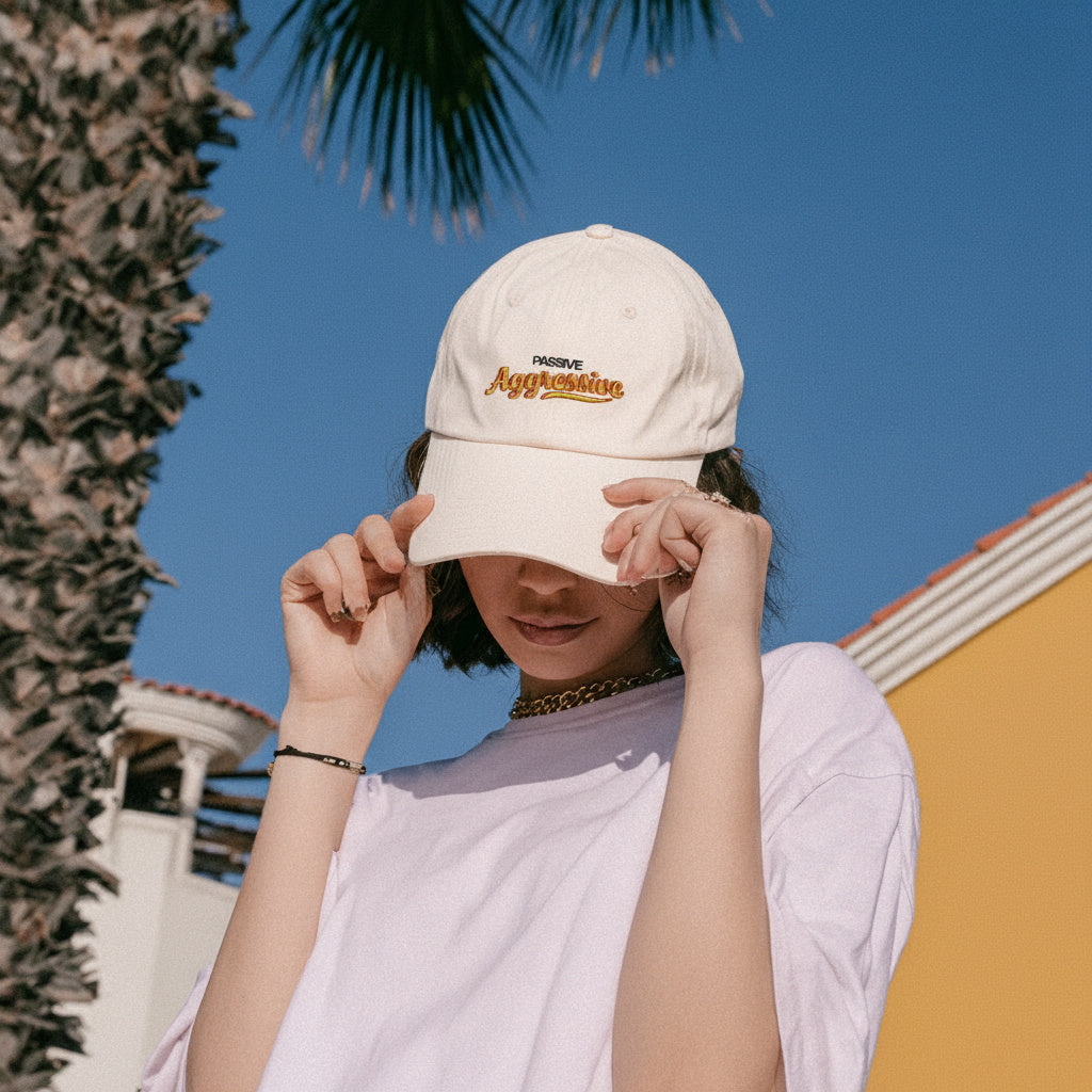 Person wearing a beige cap with text, standing outdoors against a blue sky and palm tree.