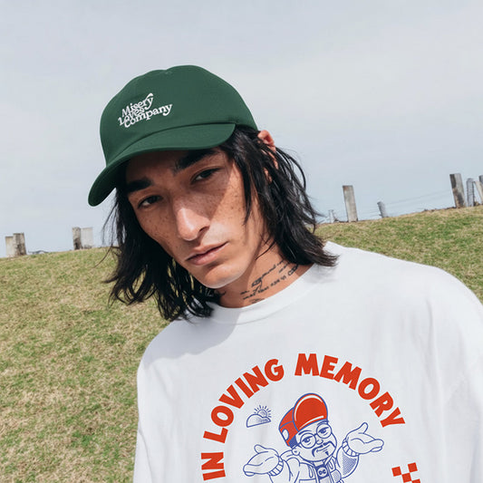 Person wearing a green cap and white sweatshirt with a graphic design outdoors