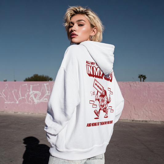 Person wearing a white hoodie with red graphics and text outdoors against a pink wall.