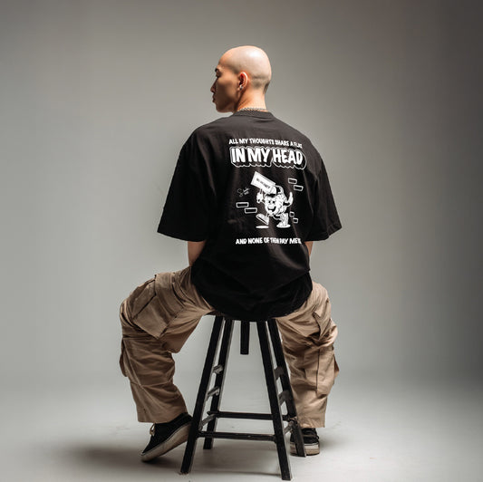 Person sitting on a stool wearing a black t-shirt with text and graphics.