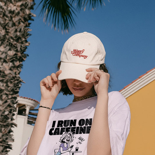 Person wearing a beige cap with text and a white t-shirt with a graphic and text, outdoors.