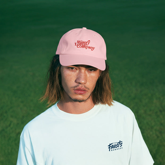 Person wearing a pink cap with text and a light blue shirt with text, standing against a green background
