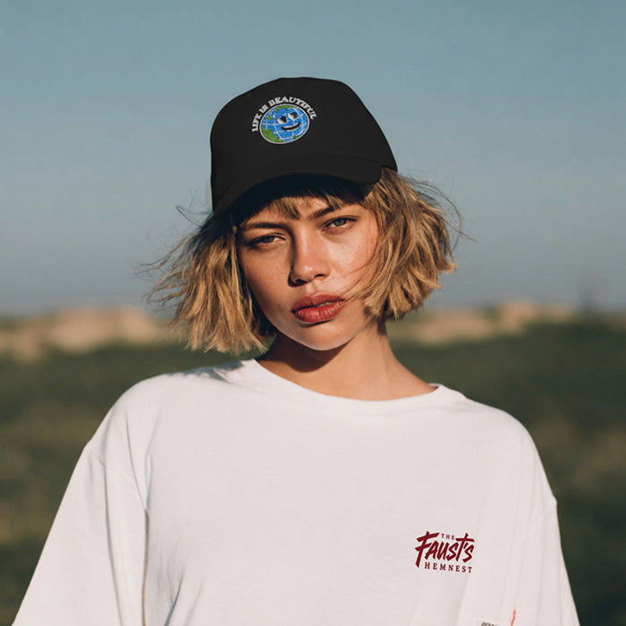 Person wearing a black cap and white t-shirt with text, standing outdoors.