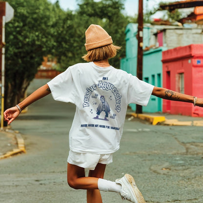Person wearing a white t-shirt with text and graphics, beige beanie, and white shorts walking on a street.