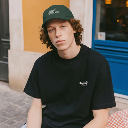 Person wearing a black t-shirt and green cap with text, sitting outdoors.