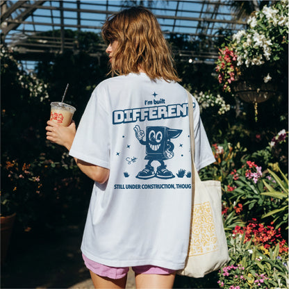 Person wearing a white t-shirt with a graphic design and text, standing in a garden.