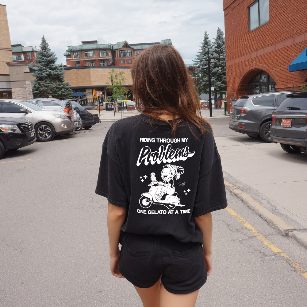 Person wearing a black t-shirt with text and graphics on the back, standing on a street.