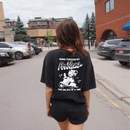 Person wearing a black t-shirt with text and graphics on the back, standing on a street.