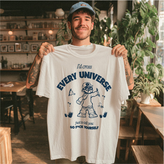 Man holding a white t-shirt with graphic design and text in a casual setting.