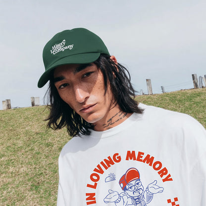 Person wearing a green cap and white sweatshirt with a graphic design outdoors