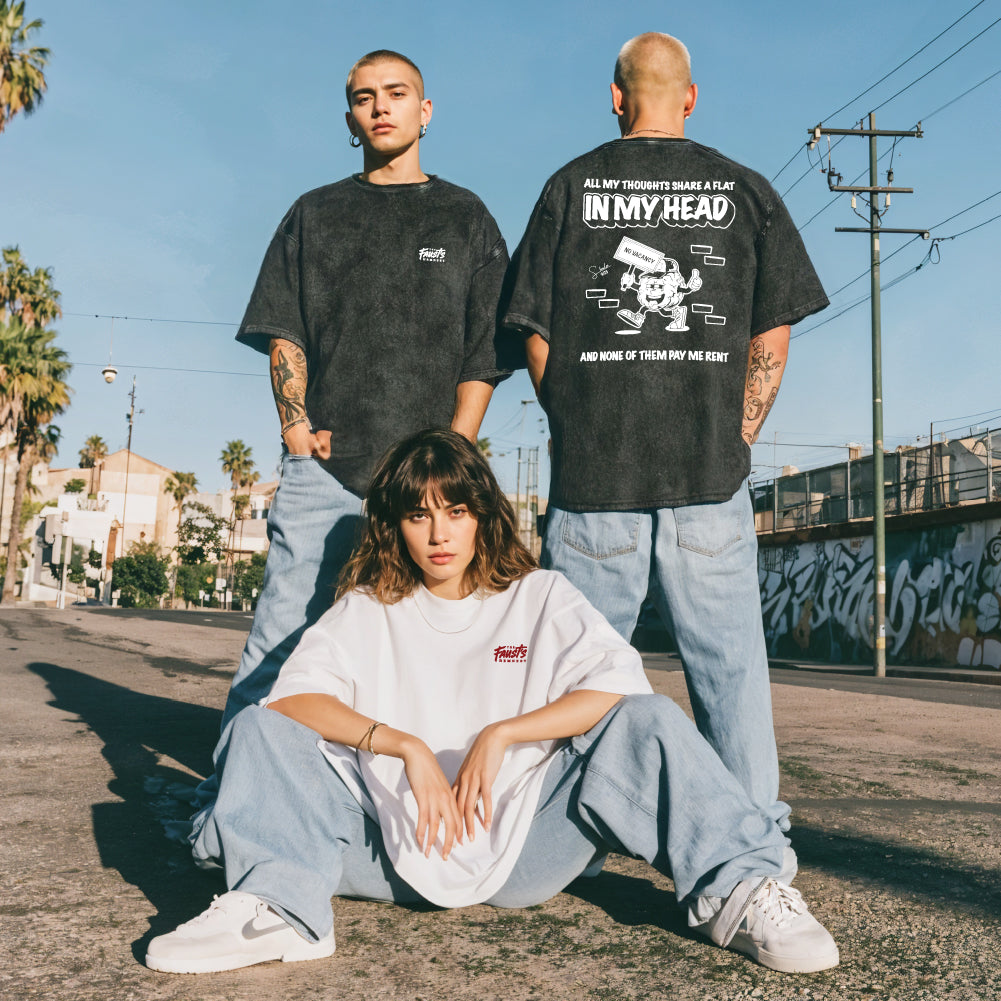 Three people wearing black t-shirts with graphic designs on a street with palm trees and graffiti.