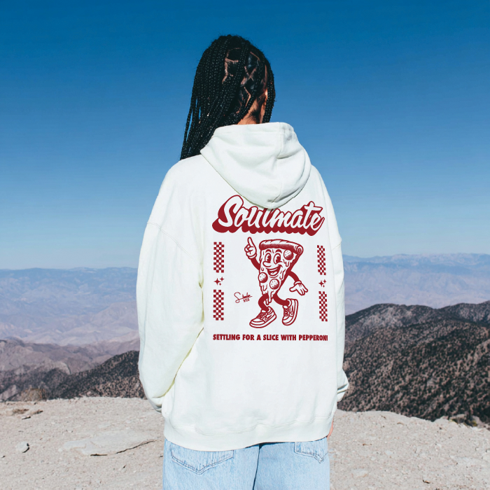 Person wearing a hoodie with a pizza graphic and text, standing on a mountain with a clear blue sky.