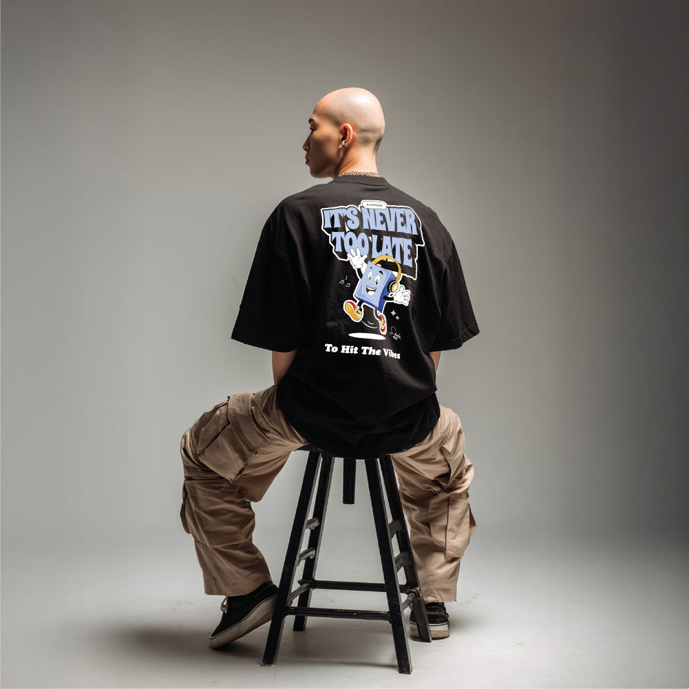 Person sitting on a stool wearing a black t-shirt with text and graphics.