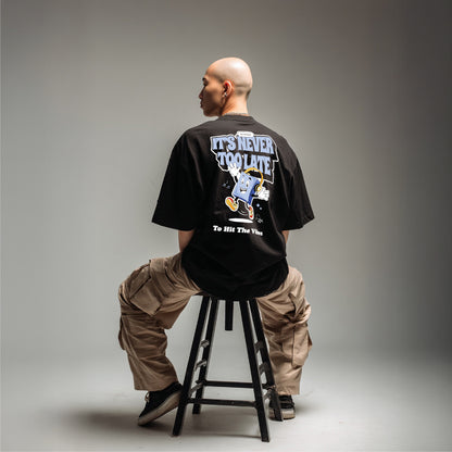 Person sitting on a stool wearing a black t-shirt with text and graphics.