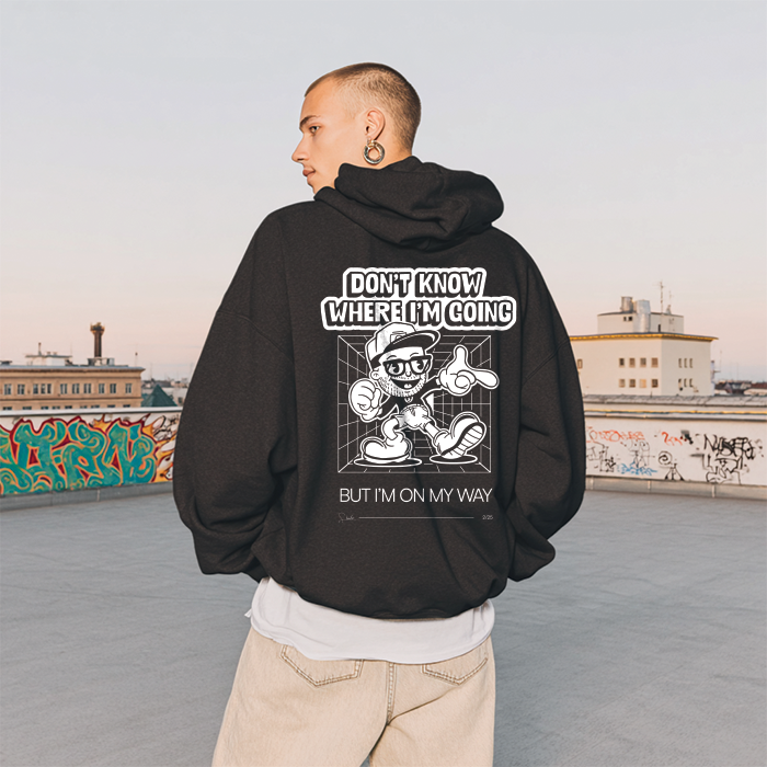 Person wearing a black hoodie with a graphic design and text on the back, standing on a rooftop with graffiti in the background.