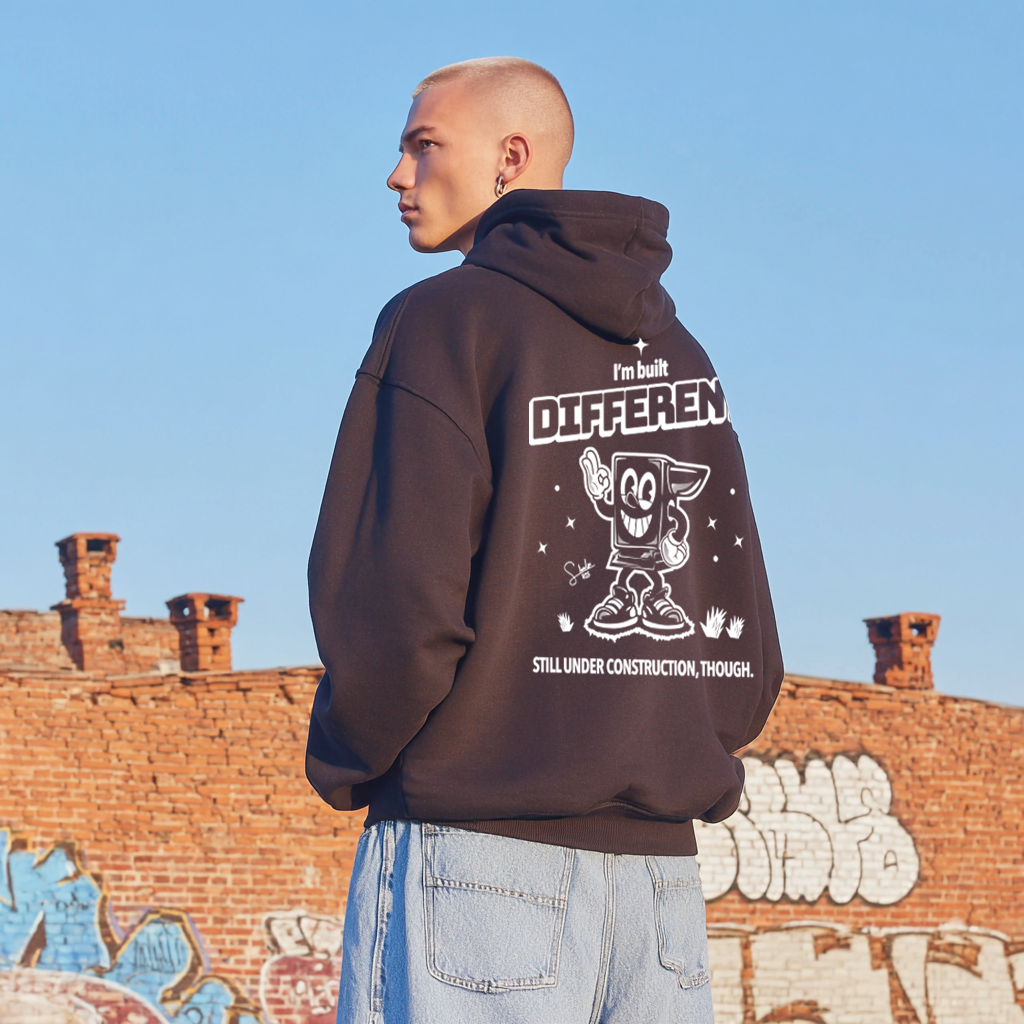 Person wearing a hoodie with text and graphics, standing against a graffiti-covered wall.